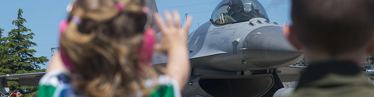 Military childern wave to Air Force jet from the tarmac.