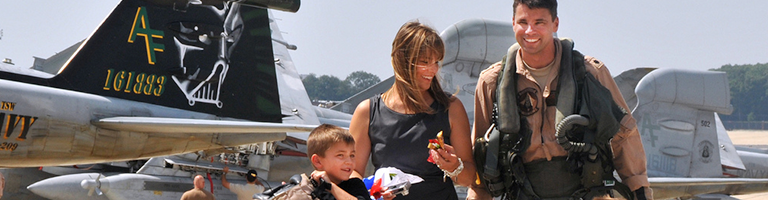 Military family walks with Air Force father on tarmac with Air Force jets in background.