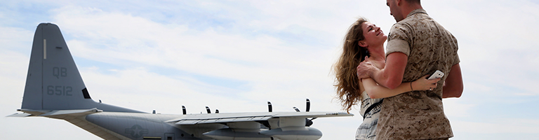 Military wife hugs husband on tarmac with United States jet in the background.